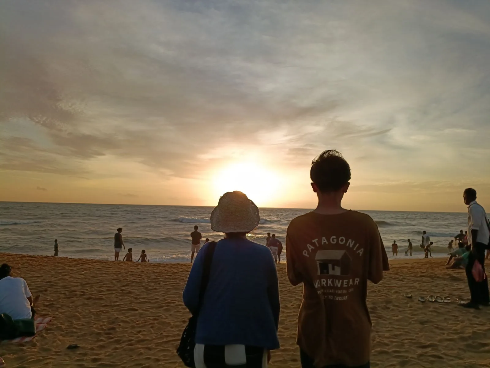夕暮れの海辺で、夕日を眺めるお客様とお孫さんの後ろ姿
